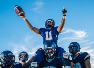 Five teenage and young adult american football players celebrating with shoulder carry