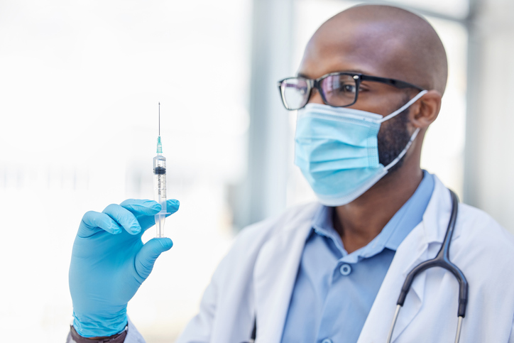 Shot of a young doctor holding a syringe filled with liquid at work