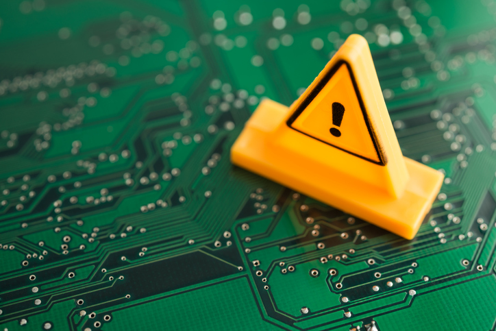 Yellow triangle emergency warning sign on green electronic circuit baord background.