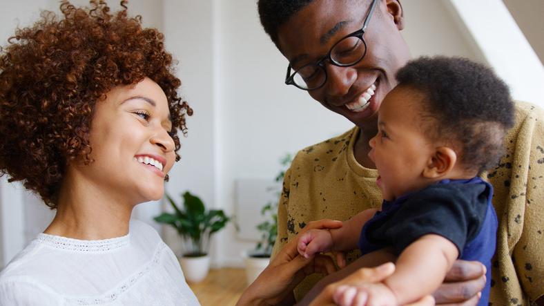 Close Up Of Loving Parents Holding Laughing Newborn Baby Son At Home In Loft Apartment
