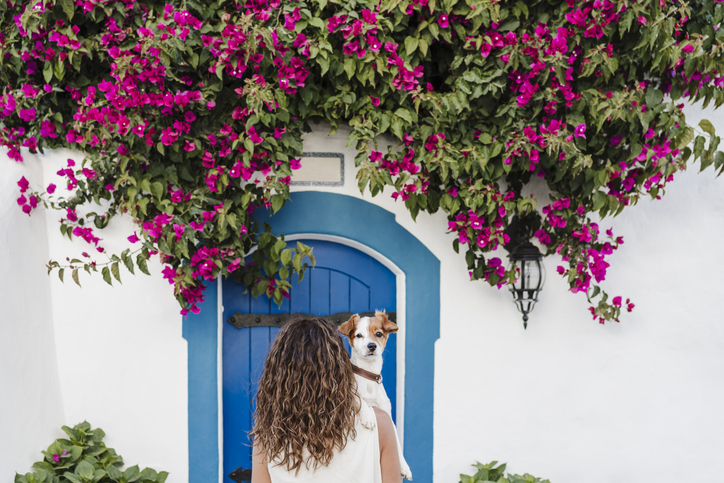 Woman with dog in front of flowering plant on wall